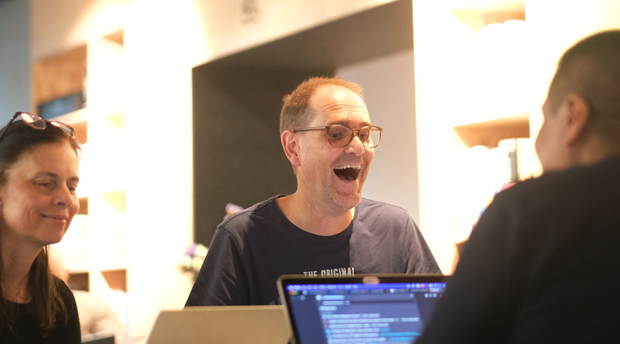 A software engineer with glasses looking ecstatic, jaw-dropped in surprise, and celebrating a coding breakthrough while collaborating over a laptop screen with a peer.